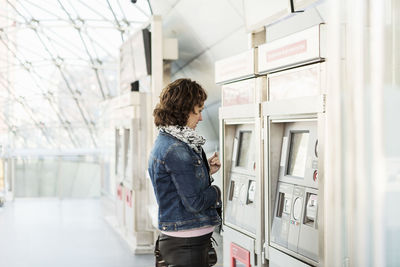 Side view of businesswoman looking at ticket machine in railway station