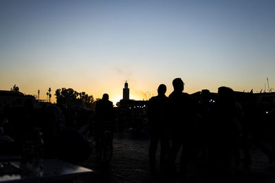 Silhouette people in city against sky during sunset