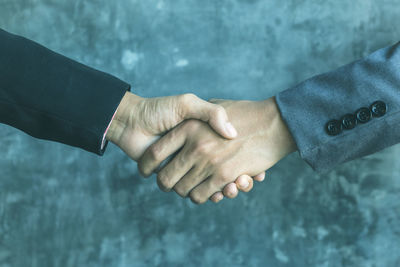 Cropped hands of businessmen shaking hands against wall