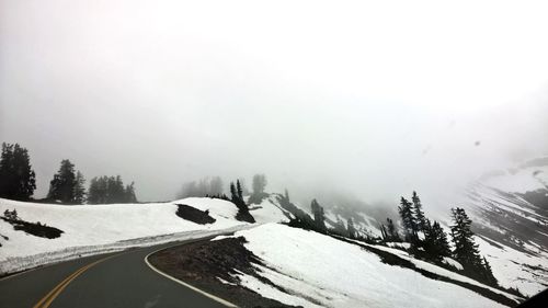 Snow covered road by trees against sky