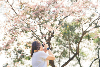 Low angle view of woman standing on pink cherry blossom tree