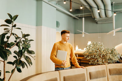 Woman looking away while sitting on potted plant at home