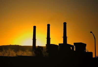 Silhouette factory against sky during sunset