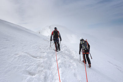 Rear view of people hiking on snowcapped mountain against sky
