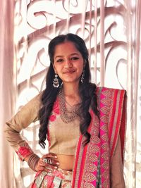 Portrait of smiling young woman standing against wall