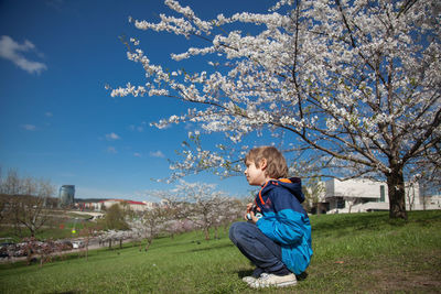 Full length of boy sitting on field against blue sky