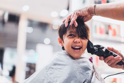 Cropped hands of barber cutting cheerful boy hair