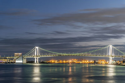 Illuminated bridge over river against sky at night