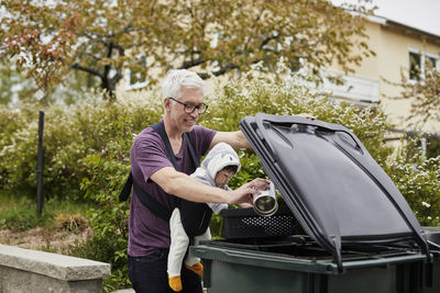 Smiling mature man with baby putting rubbish into bin