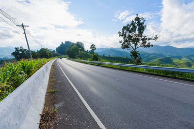 Road by trees against landscape and sky