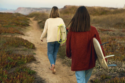 Rear view of female friends carrying surfboards at beach during sunset