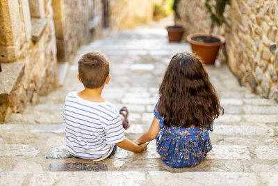 Rear view of siblings sitting on staircase outdoors