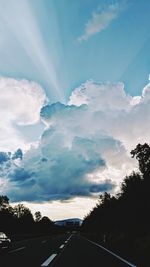 Road amidst silhouette trees against sky