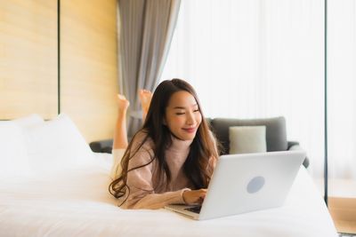 Young woman using phone while sitting on bed at home