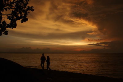 Silhouette people standing on beach against sky during sunset