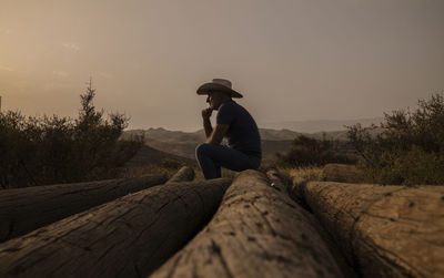 Adult man in cowboy hat sitting on tree truck in desert. almeria, spain