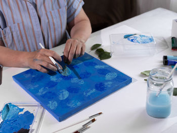 A woman paints a picture with a sheet of wood and acrylic paints