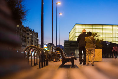 Rear view of man and woman walking on street at night