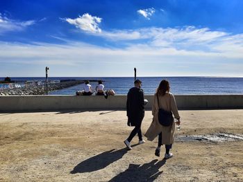 Rear view of people on beach against sky