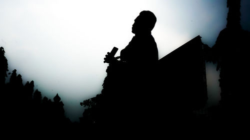 Silhouette man amidst buildings against clear sky