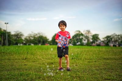 Full length of cute boy walking on grassy field against sky