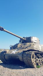 Armored tank on field against clear blue sky