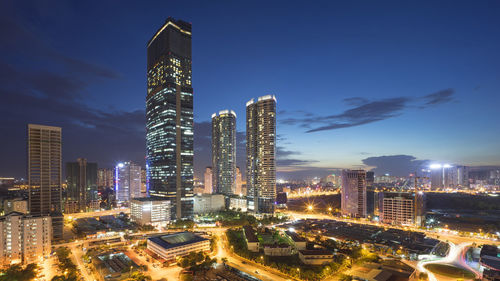 Illuminated cityscape against blue sky at night