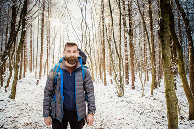 Portrait of mature man with backpack standing against snow covered trees during winter