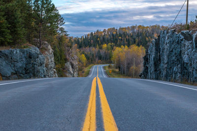 Empty country road along trees and against sky