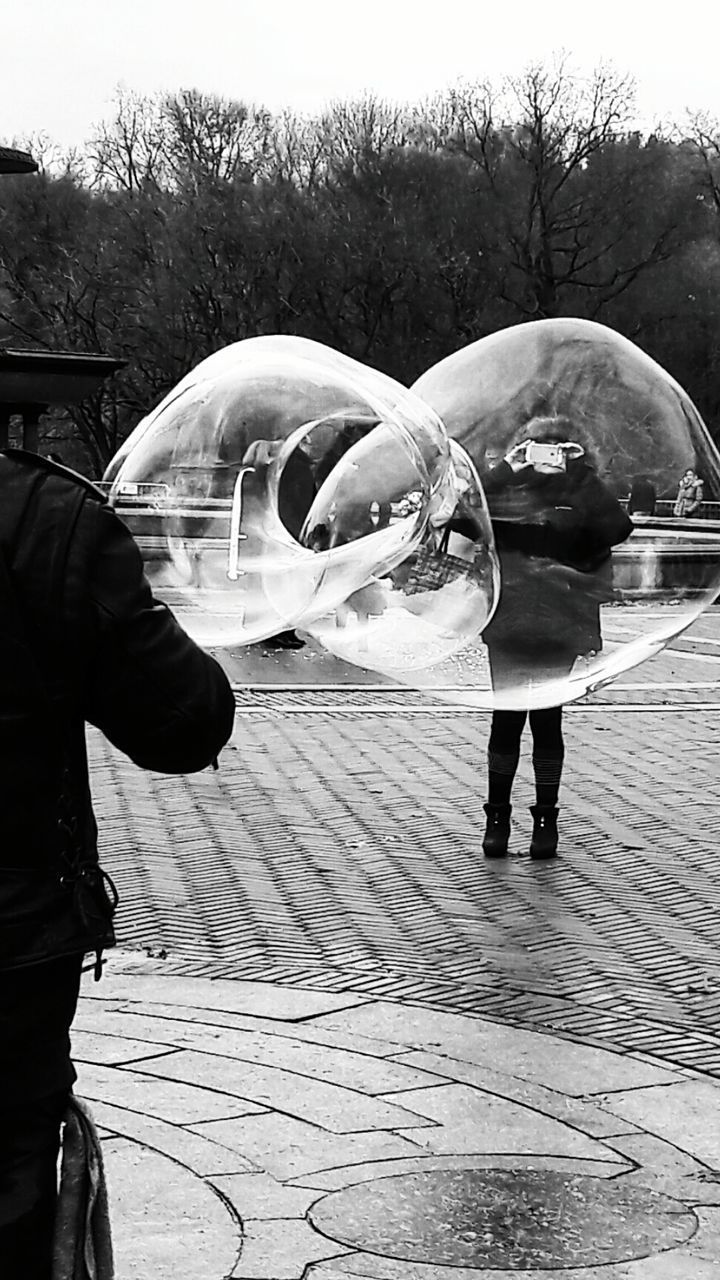 CLOSE-UP OF HAND HOLDING BUBBLES AGAINST SKY