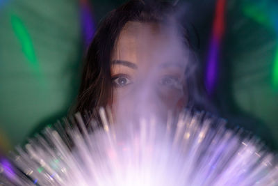 Close-up portrait of young woman holding illuminated fiber optic in darkroom