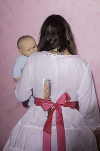 Rear view of woman with doll standing against wall