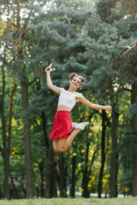 A young happy woman in a red skirt jumps high in a summer park, having fun person
