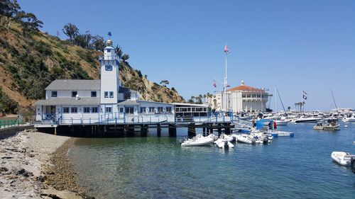 Sailboats moored on sea by buildings against clear sky