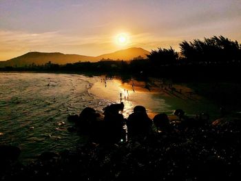 Silhouette people by lake against sky during sunset