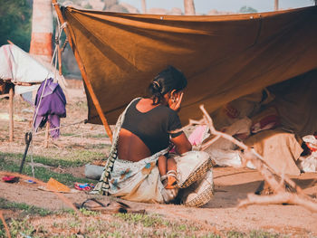 Rear view of man sitting on tent on field