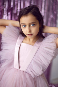 Beautiful girl with big eyes in a pink dress stands against the background of new year's tinsel