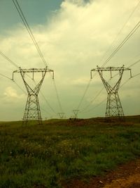 Electricity pylon on field against cloudy sky