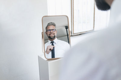 Businessman looking into mirror, fastening his tie