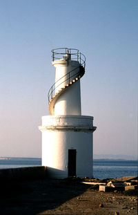 Lighthouse by sea against clear sky