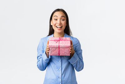 Portrait of smiling young woman holding gift box against white background