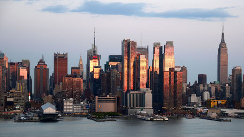 Cityscape by river against sky during sunset