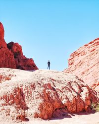 Low angle view of man standing on rock formations against clear sky