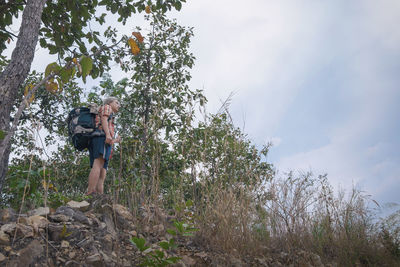 Low angle view of young man standing on rocks against cloudy sky