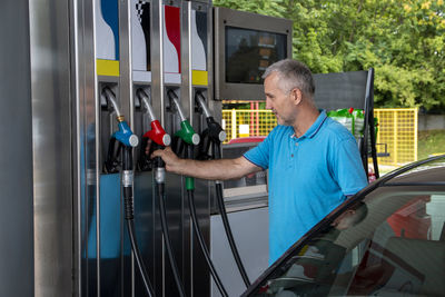 Mature man pouring petrol into tank of his vehicle on filling station. travel,transportation 