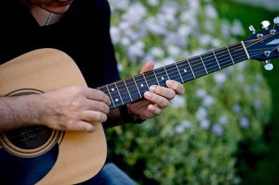 Midsection of man playing guitar while sitting outdoors