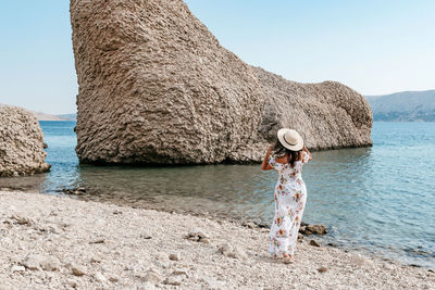 Full length rear view of woman in long dress standing on beautiful beach on pag island in croatia.