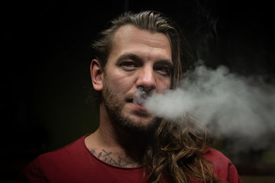 Portrait of young man smoking against black background