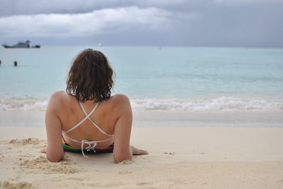 Rear view of woman relaxing at beach against sky