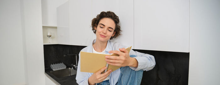 Portrait of smiling young woman using digital tablet while standing against wall
